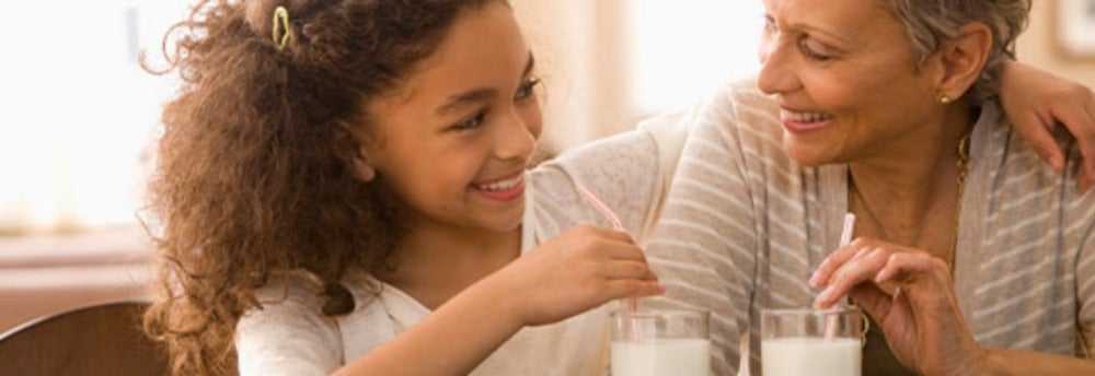 Nieta y abuela bebiendo dos vasos de leche, un alimento con calcio