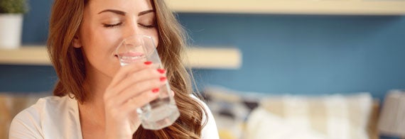 Mujer disfruta tomar agua en casa por sus diversos beneficios para la salud