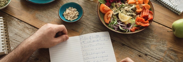 Hombre desayuna mientras anota sus progresos al comer balanceado