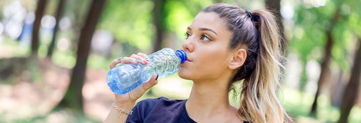 Mujer toma agua luego del ejercicio para estar hidratada y tener hábitos saludables