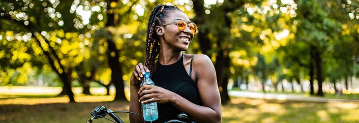 Mujer recorre el parque en bicicleta mientras toma agua porque es un nutriente esencial