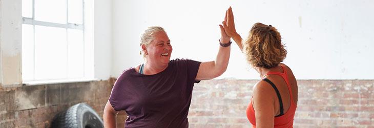Dos mujeres chocan las manos luego de hacer ejercicio al celebrar sus logros en el marco del body neutrality