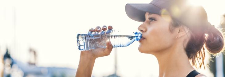 Mujer bebe agua bajo un día soleado para aplicar adecuadamente un déficit calórico