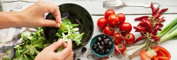 Unas manos cortan hojas de espinaca en un tazón rodeado de verduras para consumir en el marco de un déficit calórico