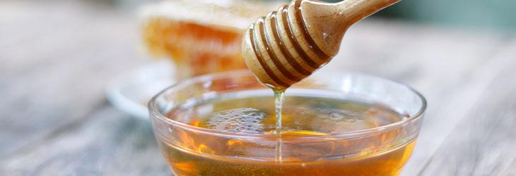 Cucharón y taza de miel, considerada un edulcorante natural, sobre una mesa de madera