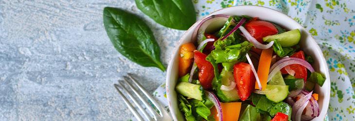 Consume vegetales en ensalada que incluye espinaca, tomate, cebolla y pepino 