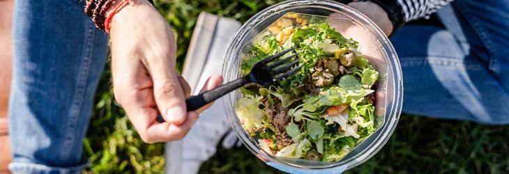 Una persona comiendo una ensalada de espinaca y lechuga, alimentos fuentes de vitaminas liposolubles