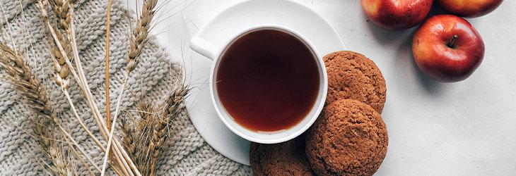 Taza de té acompañada de galletas integrales de salvado y cinco manzanas sobre una mesa