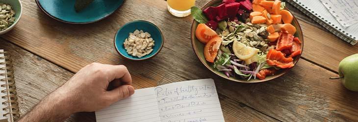 Hombre lista alimentos para dienta hipocalórica. A su lado un plato de frutos secos y verdura 