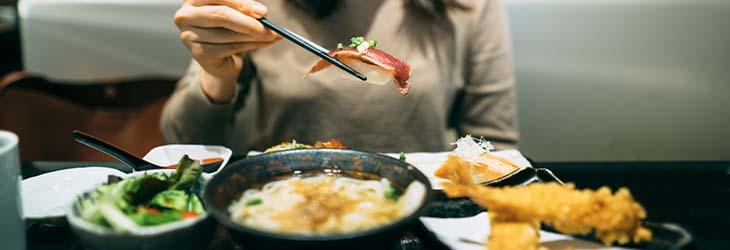 Mujer come sushi, sopa de udon y tempura de mariscos que son alimentos con zinc
