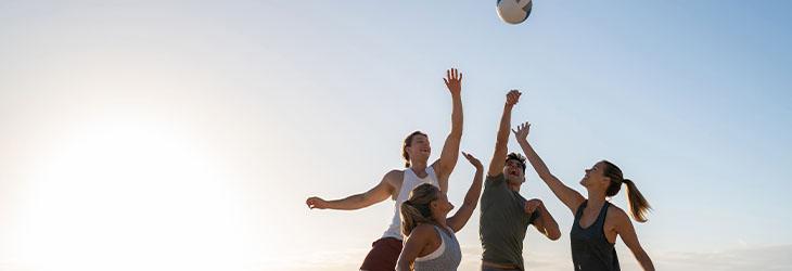 Para construir relaciones sociales, grupo de personas juega vóleibol playa en un día soleado