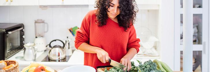 Mujer cocina platillos con frutas y verduras para seguir una dieta vegetariana