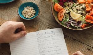 Hombre desayuna mientras anota sus progresos al comer balanceado