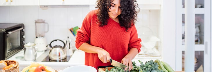 Mujer cocina platillos con frutas y verduras para seguir una dieta vegetariana 